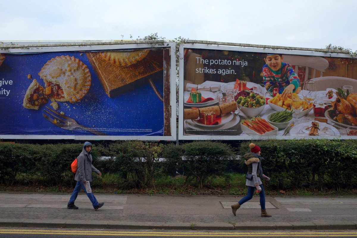 People walking by in front of large billboards advertising Christmas food and groceries. Copyright: Thinglass | Shutterstock