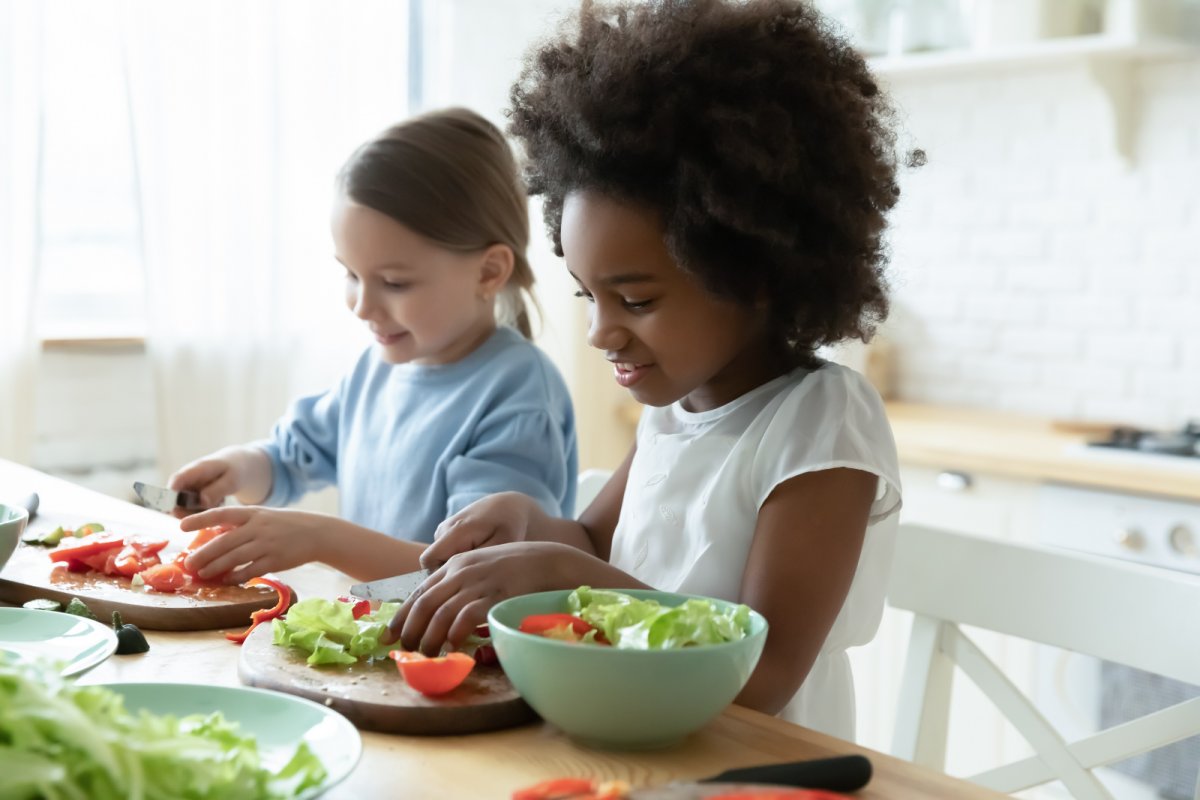Two young girls chopping up vegetables. Copyright: fizkes | shutterstock
