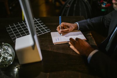 A person writing in a notebook at a desk . Credit: RDNE Stock